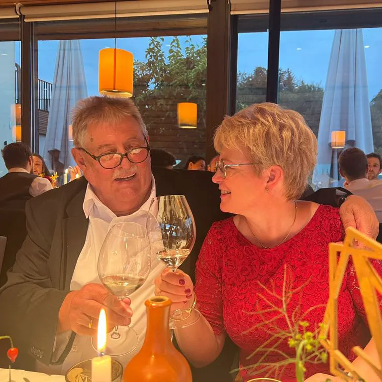 Ein Paar stößt bei einem festlichen Abendessen mit Weingläsern an und lächelt sich an – ein Moment voller Herzlichkeit und Lebensfreude am Rasdorferhof