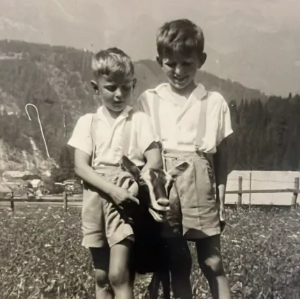 Altes Schwarz-Weiß-Foto von zwei Buben der Familie Hopfgartner auf einer Wiese am Bauernhof im Kärntner Drautal, die gemeinsam eine Ziege halten – eine Erinnerung an die frühen Jahre am Rasdorferhof