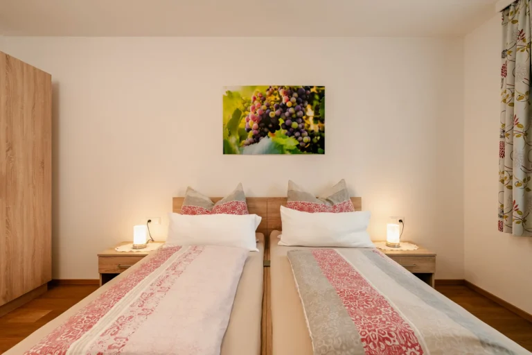 Das gemütliches Doppelzimmer "Weinrebe" im Rasdorferhof Kärnten mit hochwertigen Einzelbetten, rot-weißer Bettwäsche und liebevoller Einrichtung.