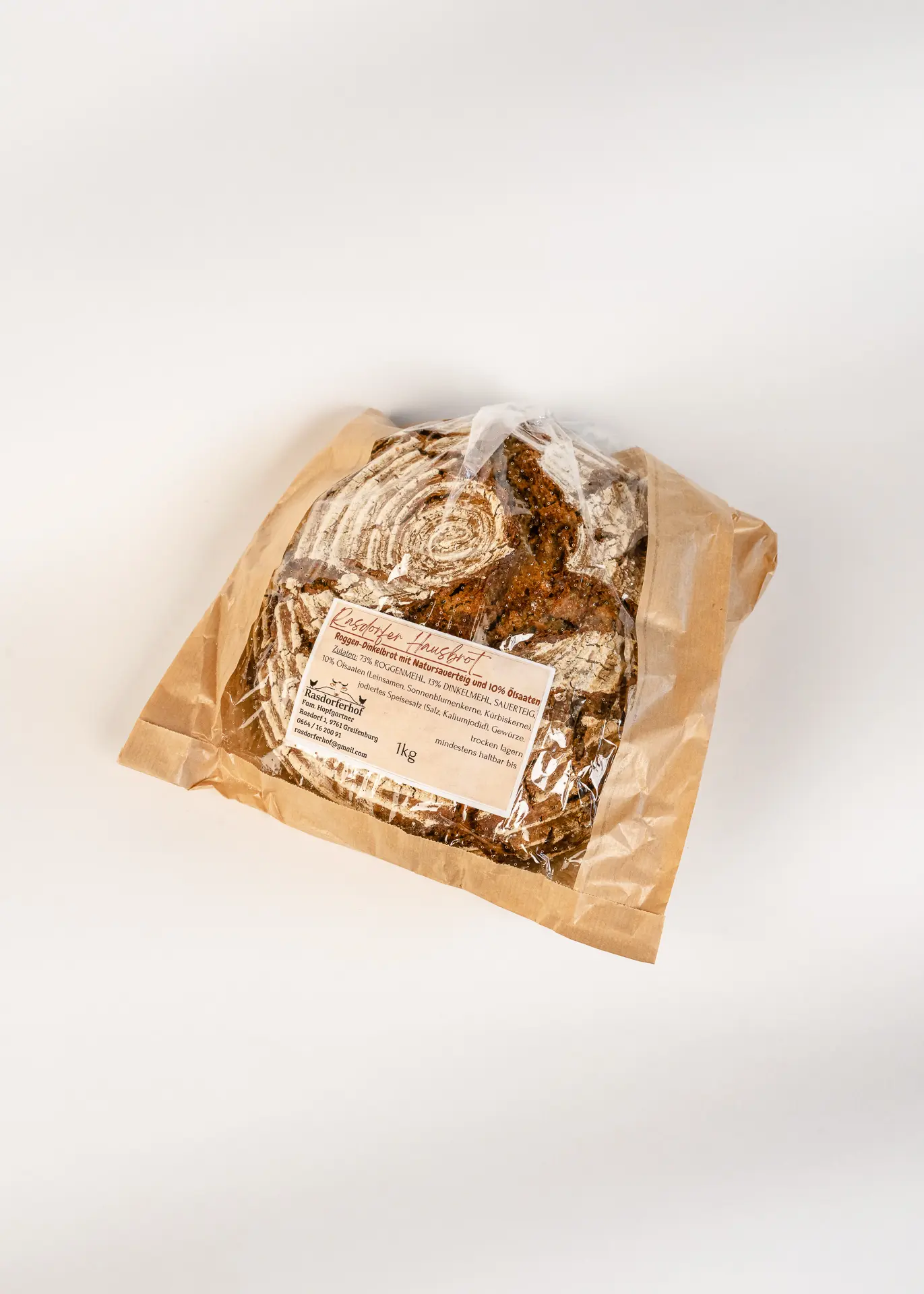 Ein rundes Bauernbrot vom Rasdorferhof liegt bemehlt in braunem Papier mit Etikett und steht für nachhaltige Qualität.