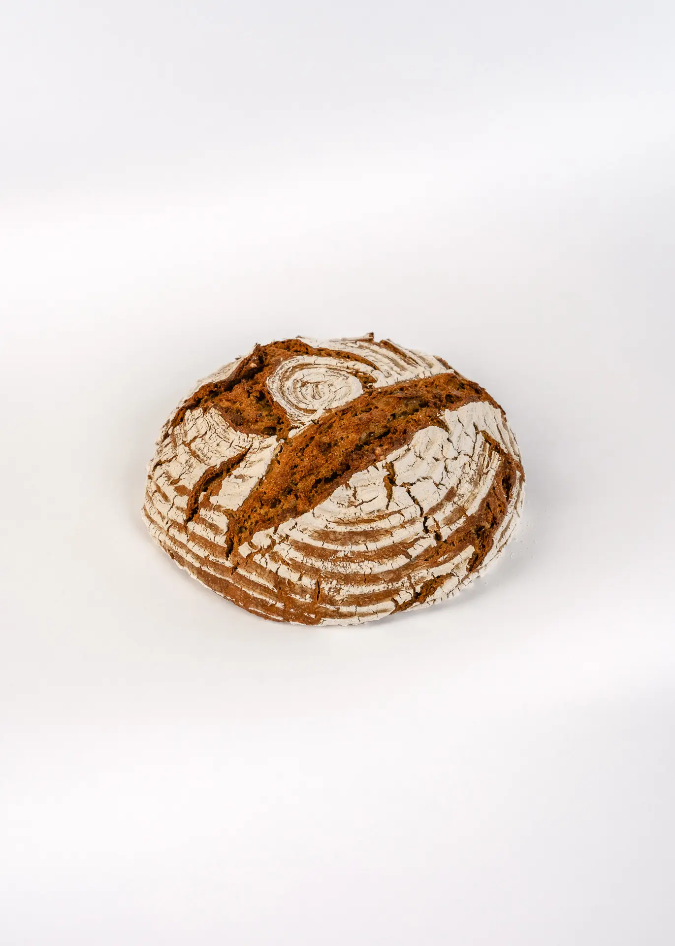 Ein rundes Bauernbrot vom Rasdorferhof in Kärnten liegt auf weißem Untergrund. Die bemehlte Kruste zeigt tiefe Risse. | Bauernbrot kaufen