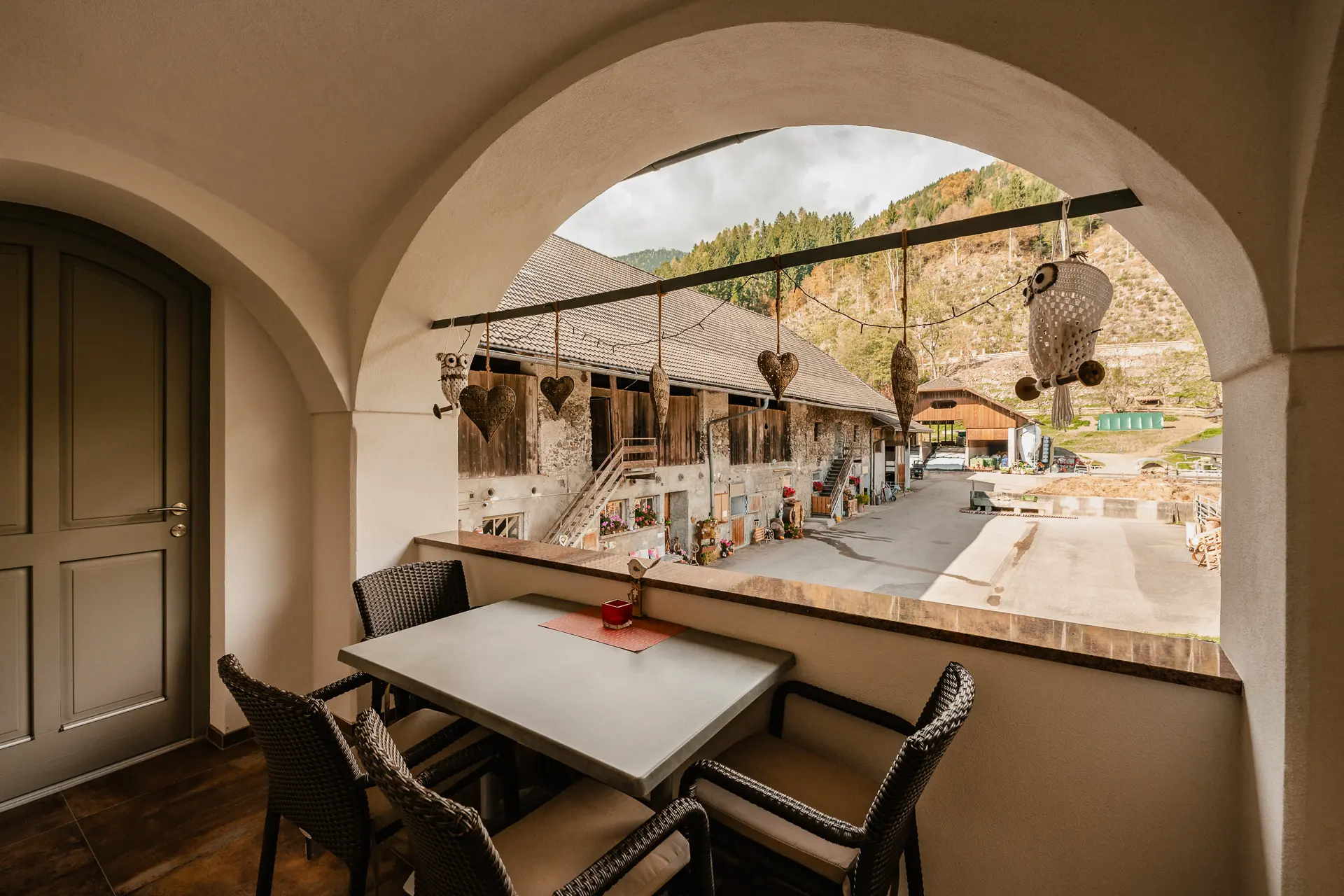 Überdachter Balkon am Rasdorferhof in Kärnten mit Tisch und vier Stühlen bietet Ausblick auf Innenhof, Scheunen und Berge. So schön ist Urlaub am Bauernhof.