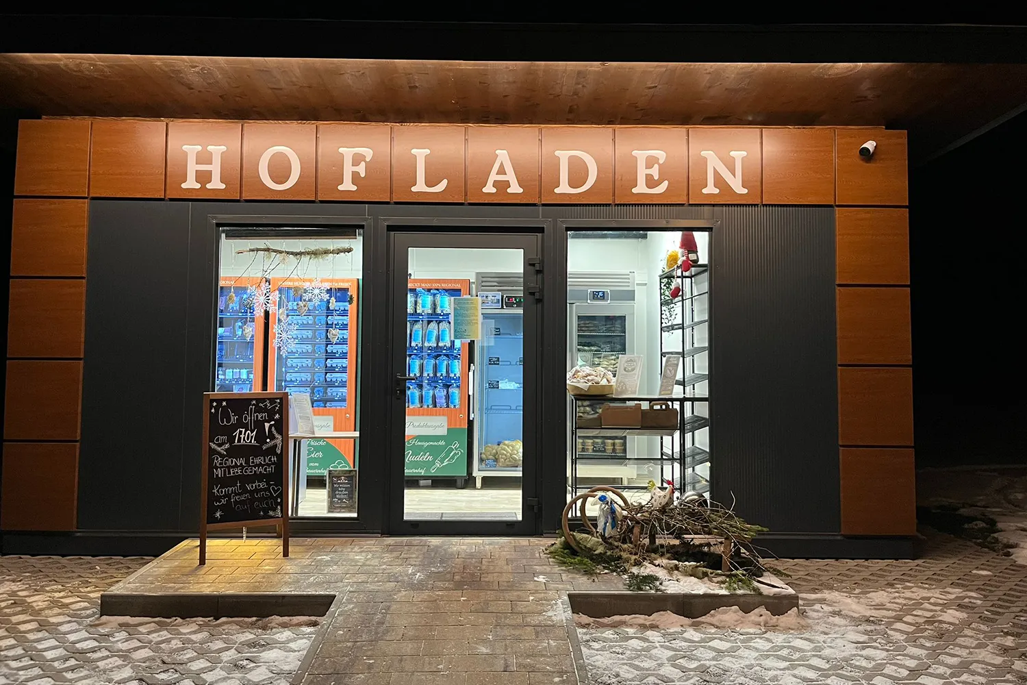 Außenansicht des Rasdorferhof Hofladens bei Nacht mit moderner Holzfassade und beleuchtetem Eingangsbereich